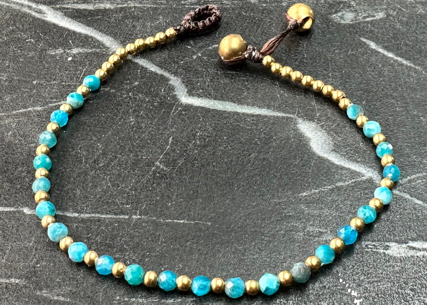 A crystal healing bracelet made of faceted Blue Apatite crystals on a cotton cord with brass beads.