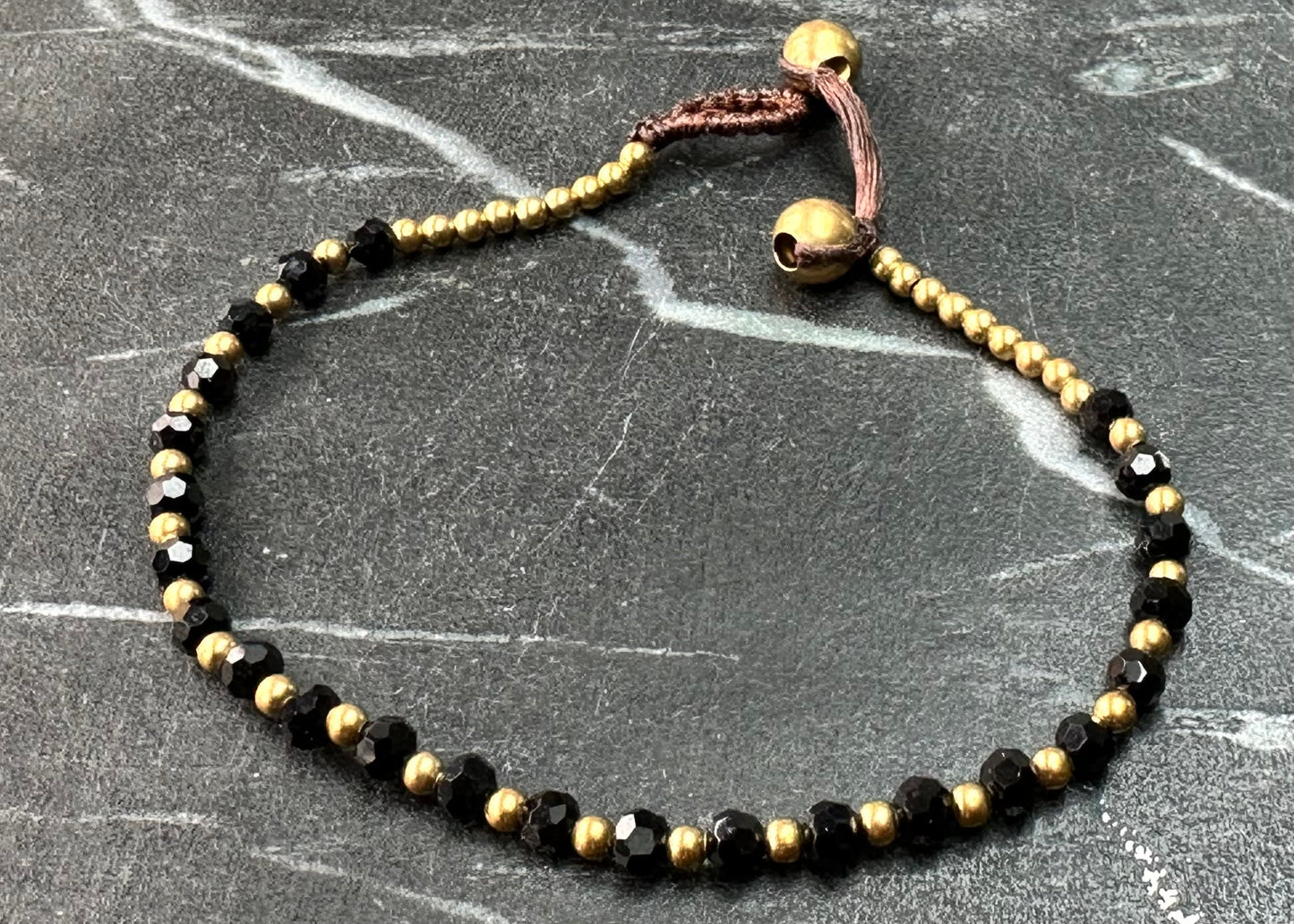 A crystal healing bracelet made of faceted Black Spinel crystals on a cotton cord with brass beads.