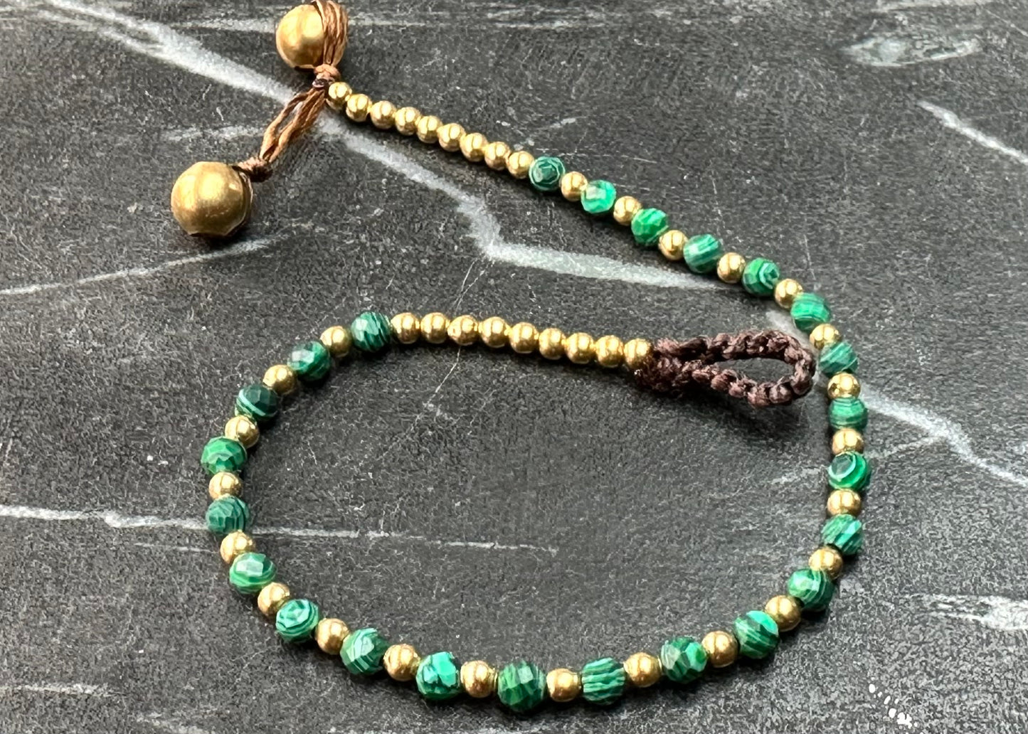A crystal healing bracelet made of faceted Malachite crystals on a cotton cord with brass beads