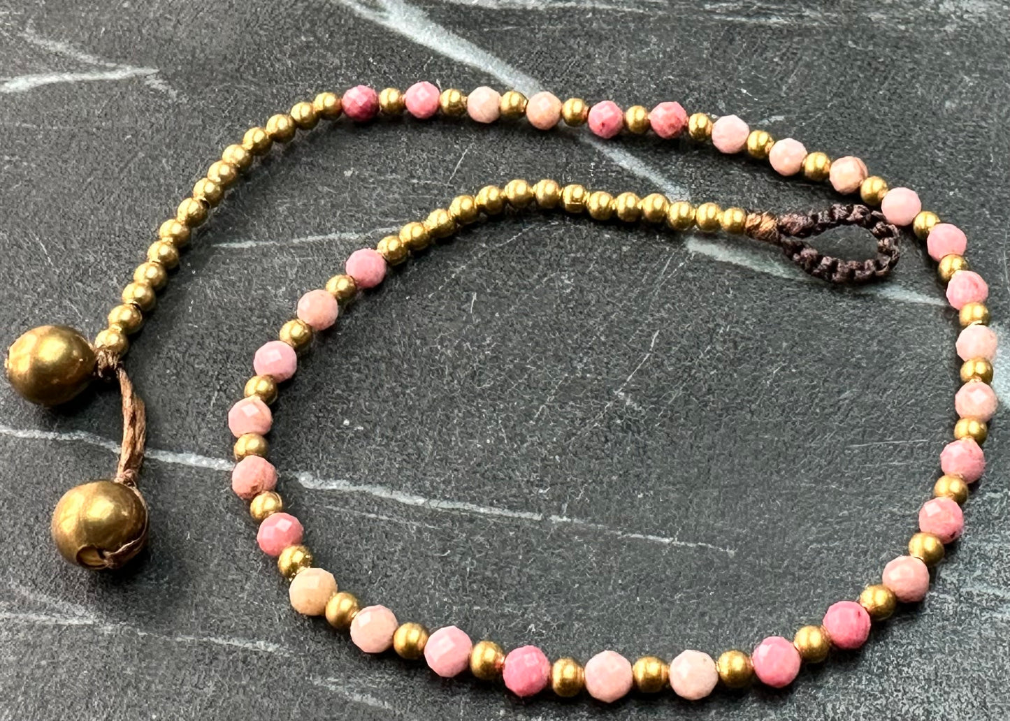 A crystal healing anklet made of faceted Pink Tourmaline crystals on a cotton cord with brass beads