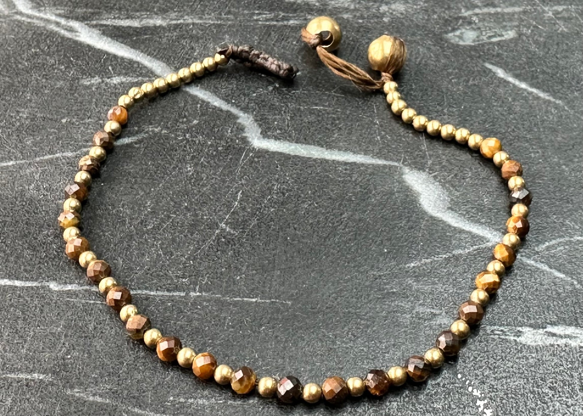 A crystal healing bracelet made of faceted Tigers Eye crystals on a cotton cord with brass beads