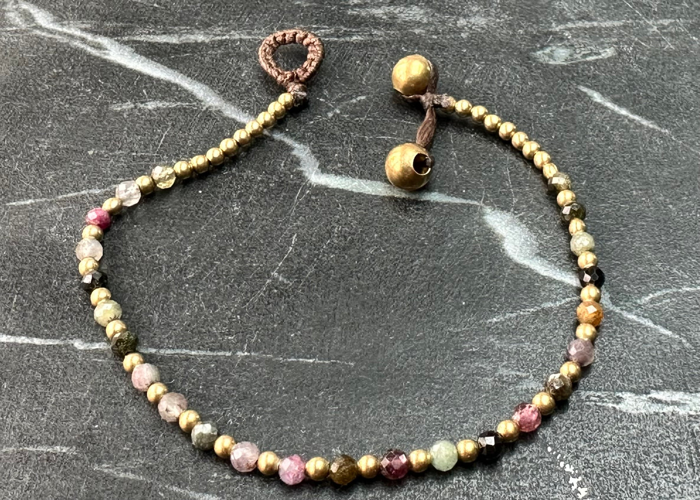 A crystal healing bracelet made of faceted Rhodonite crystals on a cotton cord with brass beads