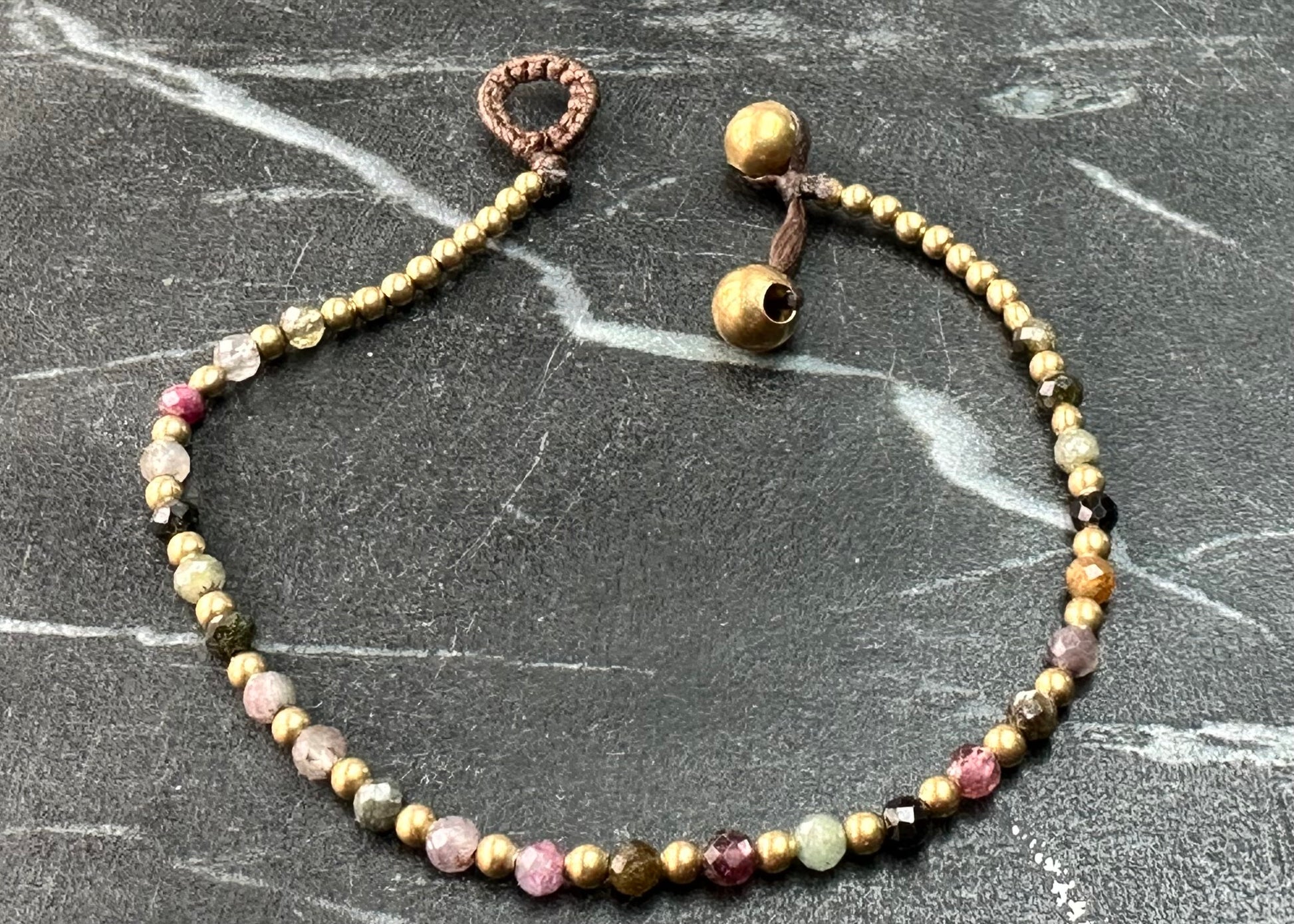 A crystal healing bracelet made of faceted Rhodonite crystals on a cotton cord with brass beads