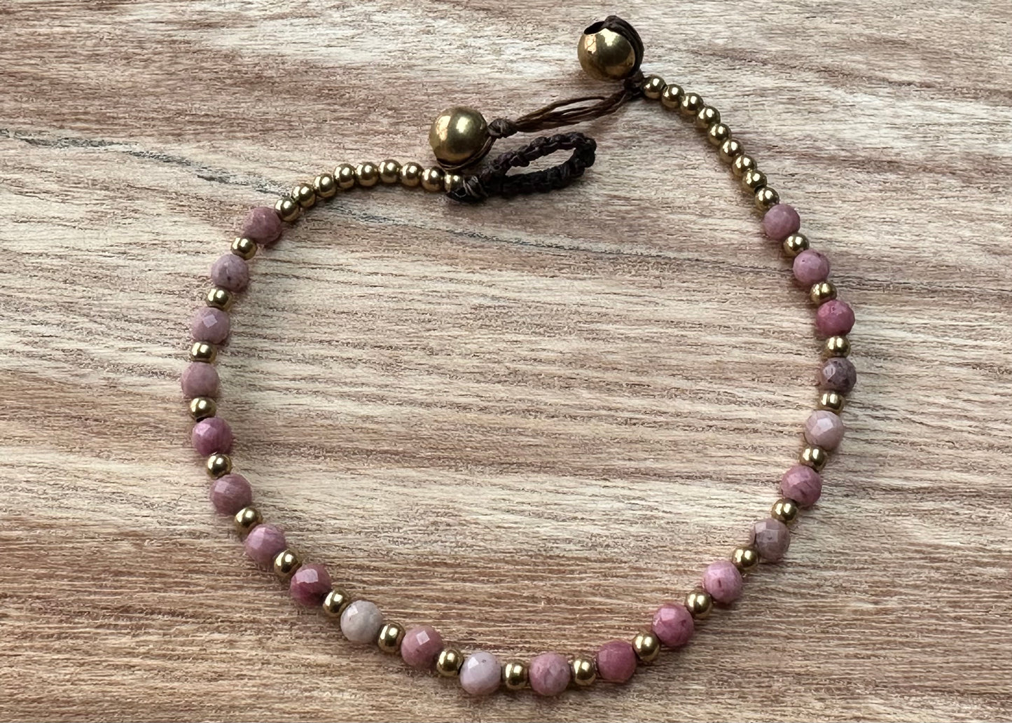A crystal healing bracelet made of faceted Rhodonite crystals on a cotton cord with brass beads