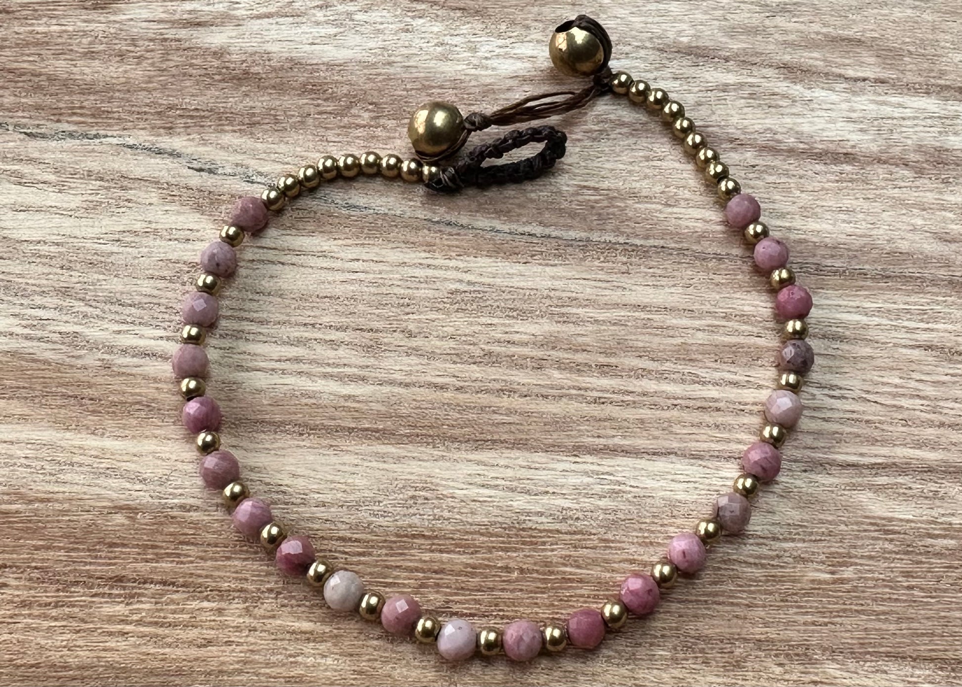 A crystal healing bracelet made of faceted Rhodonite crystals on a cotton cord with brass beads