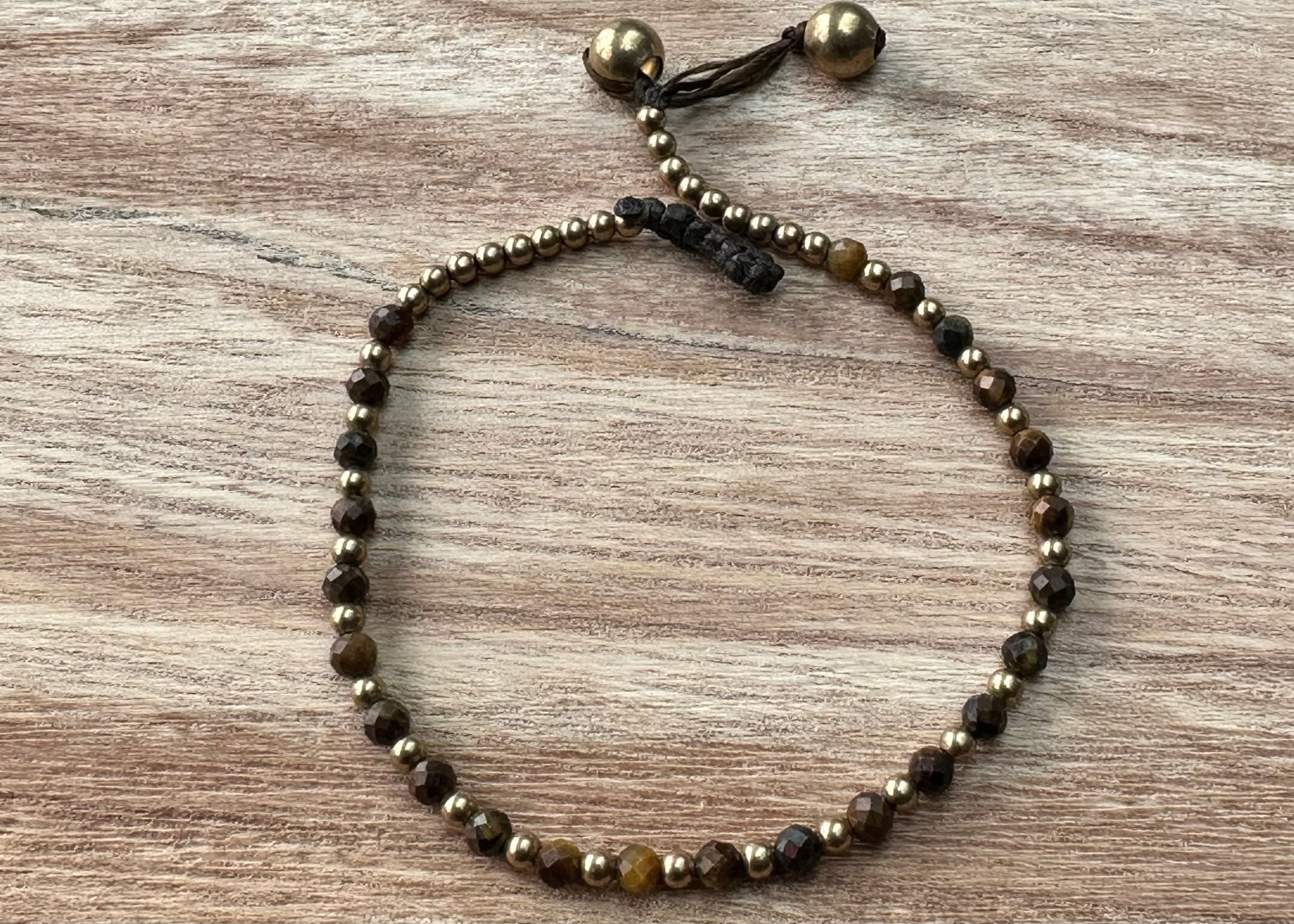 A crystal healing bracelet made of faceted Tigers Eye crystals on a cotton cord with brass beads
