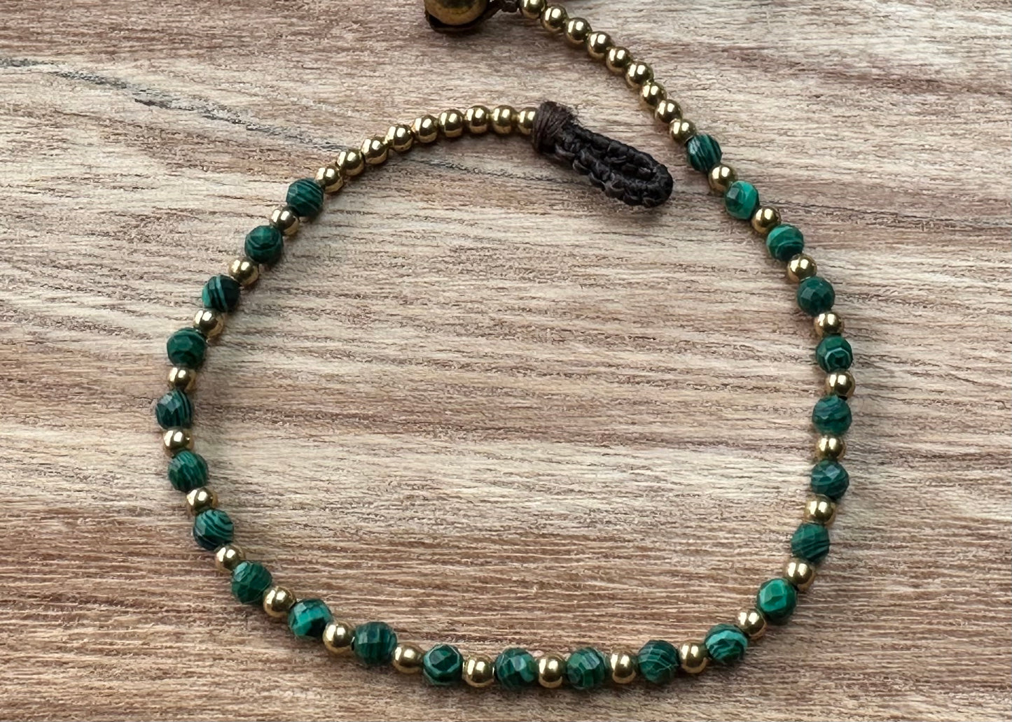 A crystal healing bracelet made of faceted Malachite crystals on a cotton cord with brass beads
